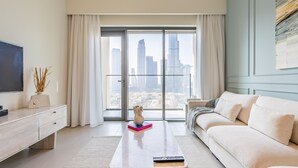 A modern living room with a sofa, a coffee table, a TV, and a view of tall buildings through large windows. - Eloquent Upscale with Breathtaking Burj (Dubai)