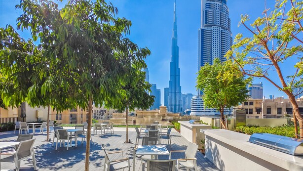 An outdoor patio with tables and chairs, trees, and a view of the Burj Khalifa. - Eloquent Upscale with Breathtaking Burj (Dubai)