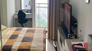 A hotel room with a bed, a desk with a chair, a TV, and a window with curtains. - Capital O 93529 September House (Tangerang)
