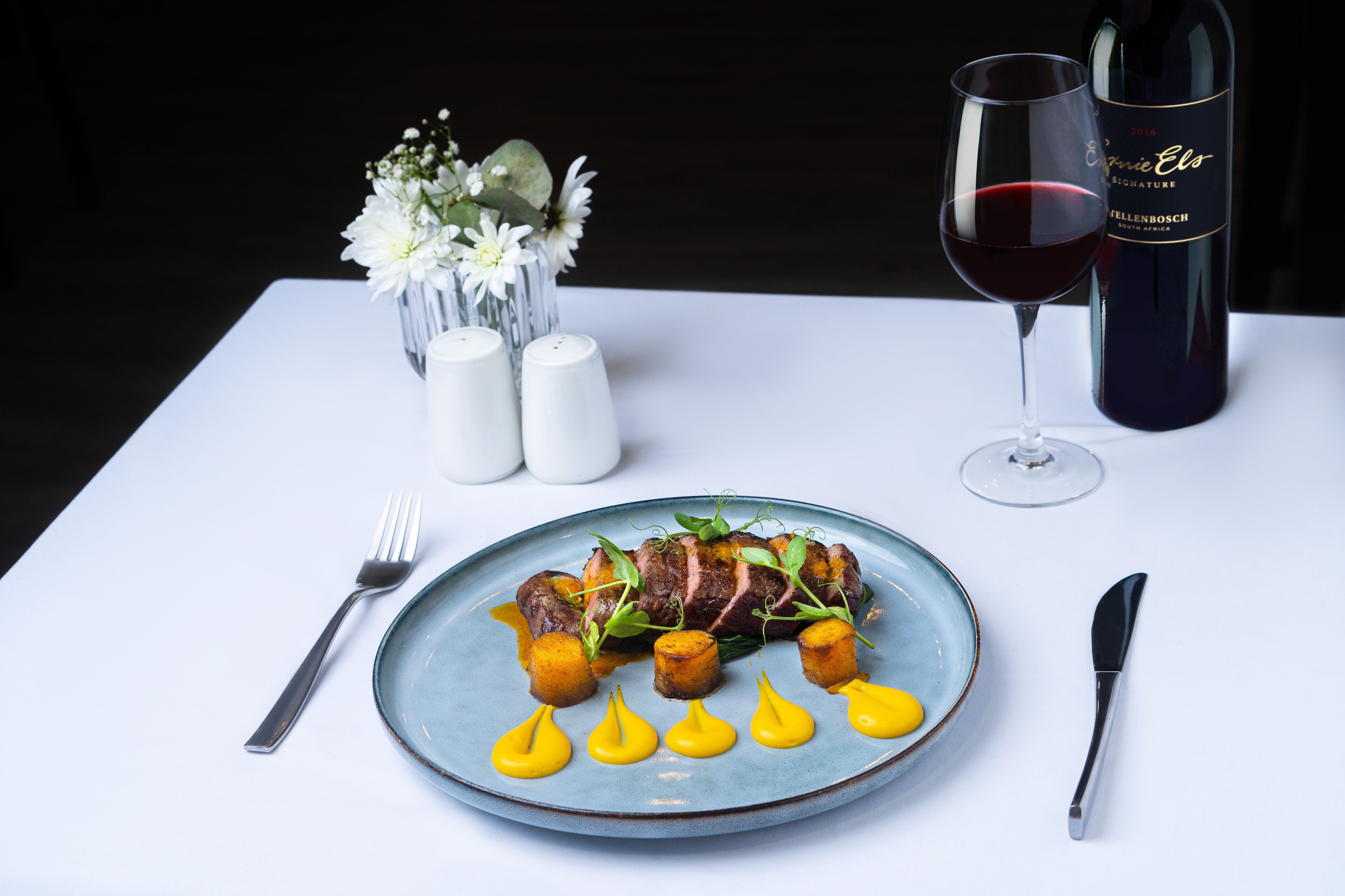 A plate of food with a glass of red wine and a bottle of wine on a table.