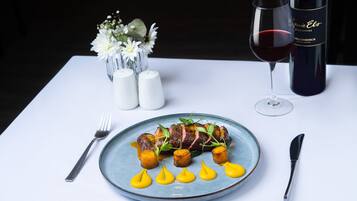 A plate of food with a glass of red wine and a bottle of wine on a table.