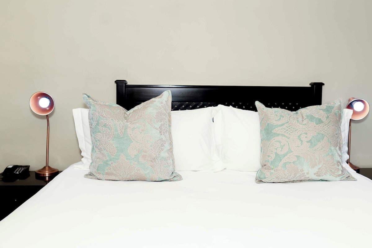 A bed with two decorative pillows, a bedside lamp, and a phone on a nightstand.