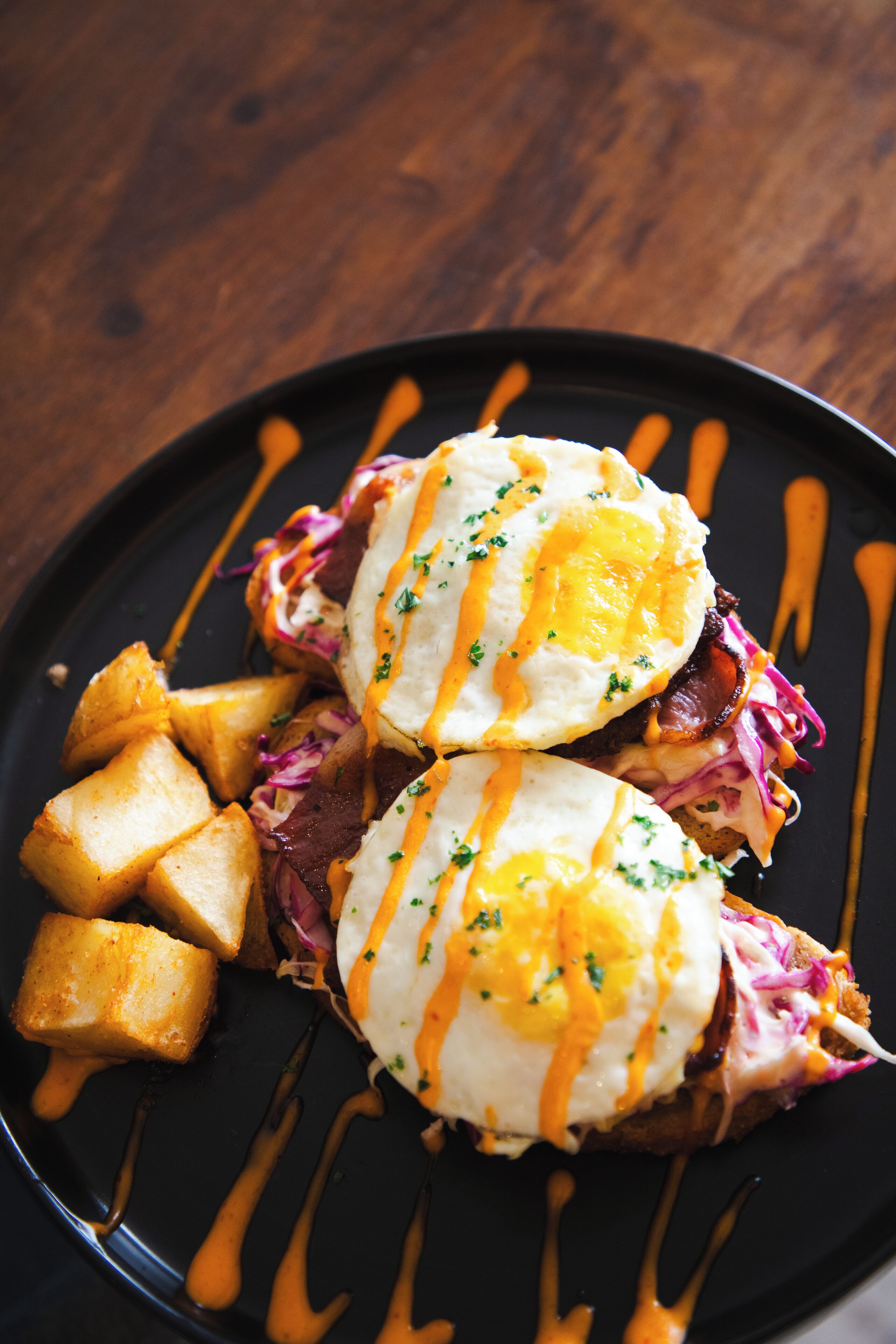 A plate with two eggs benedict sandwiches, hash browns, and a drizzle of sauce.