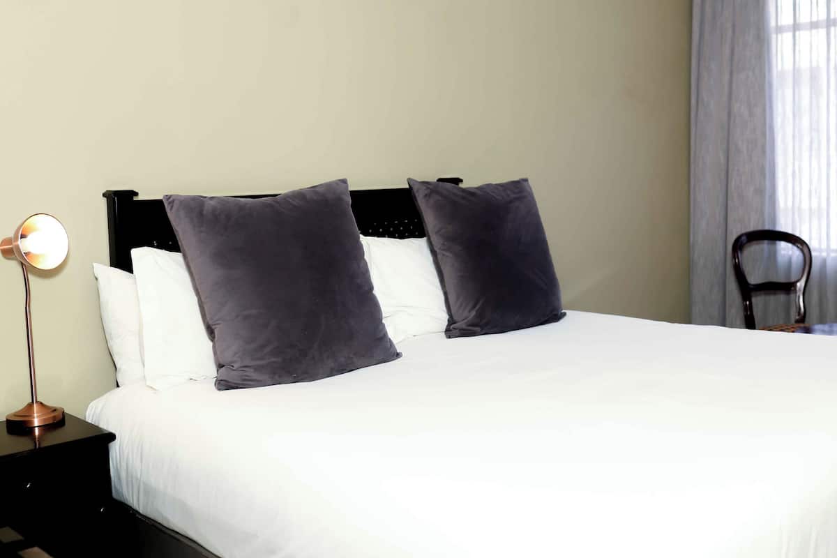 A hotel room with a bed, two pillows, a nightstand with a lamp, and a chair.