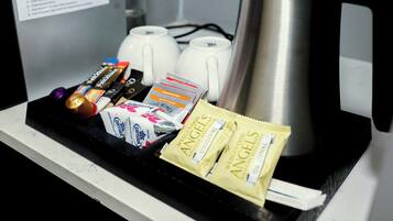 Una bandeja con diversos objetos, como un control remoto, paquetes de aperitivos y una cafetera.