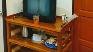 A wooden TV stand with a television, a glass of orange drink, and a plate with a cup. - Metha Country View Homestay Singburi (Khai Bang Rachan)