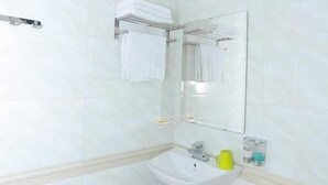 A bathroom with white tiles, a sink, a mirror, and a towel rack. - Thuy Ngu by Bay Luxury (Hanoi)