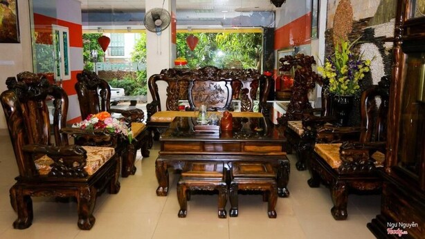 A traditional wooden furniture store with ornate chairs and tables, a fan, and a view of greenery outside. - Thuy Ngu by Bay Luxury (Hanoi)