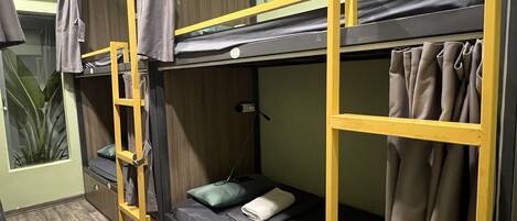 A bunk bed room with a wooden wardrobe, a small table, and a potted plant.