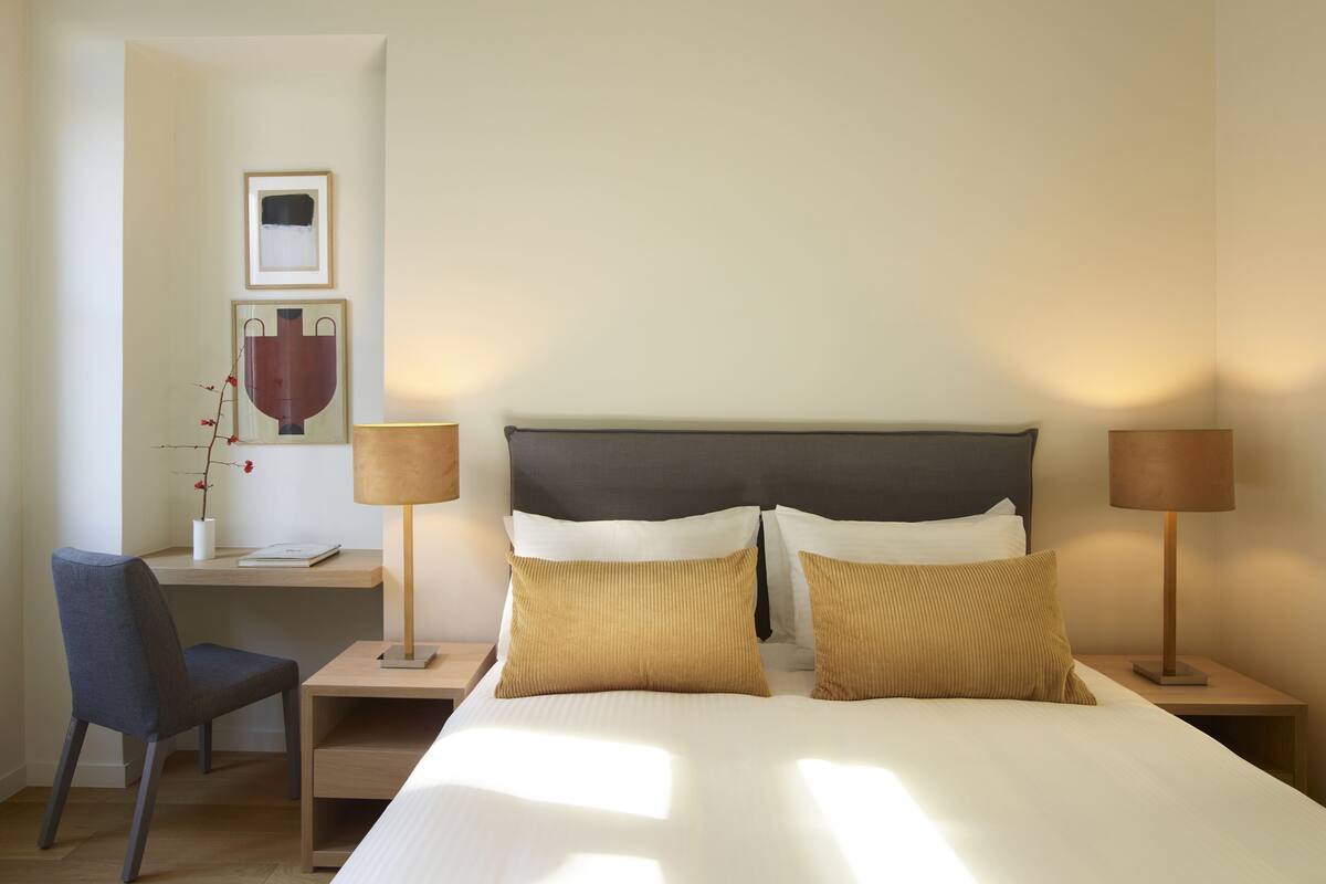 A hotel room with a bed, two bedside tables, a chair, a desk, and a lamp.