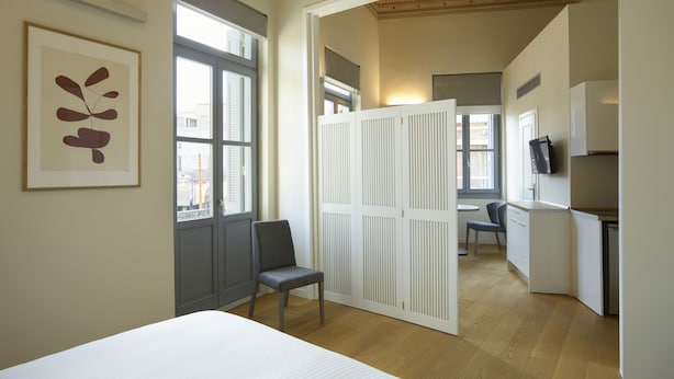 Un dormitorio con cama, una silla, un escritorio y una kitchenette.