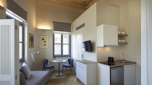 Un espacio habitable compacto con kitchenette, comedor para dos sillas, un sofá y una pequeña mesa.