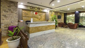 A reception area with a marble floor, a reception desk with a clock, and a seating area with chairs and a potted plant. - Dream Hotel by Bay Luxury (Hanoi)