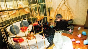 A room with a bed in a cage-like structure, a hanging chair, and scattered heart-shaped balloons on the floor. - Dream Hotel by Bay Luxury (Hanoi)