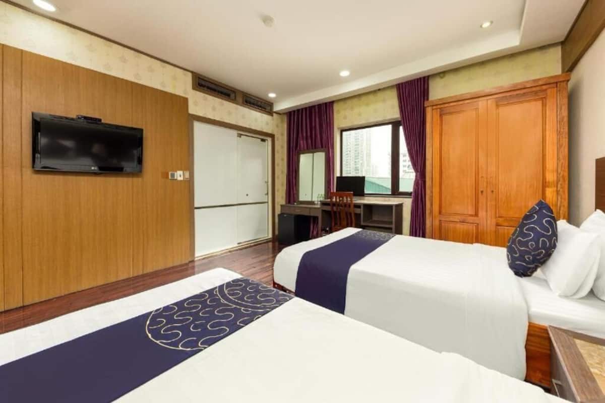 Ein Hotelzimmer mit zwei Betten, einem Schreibtisch, einem Fernseher und einem Kleiderschrank.