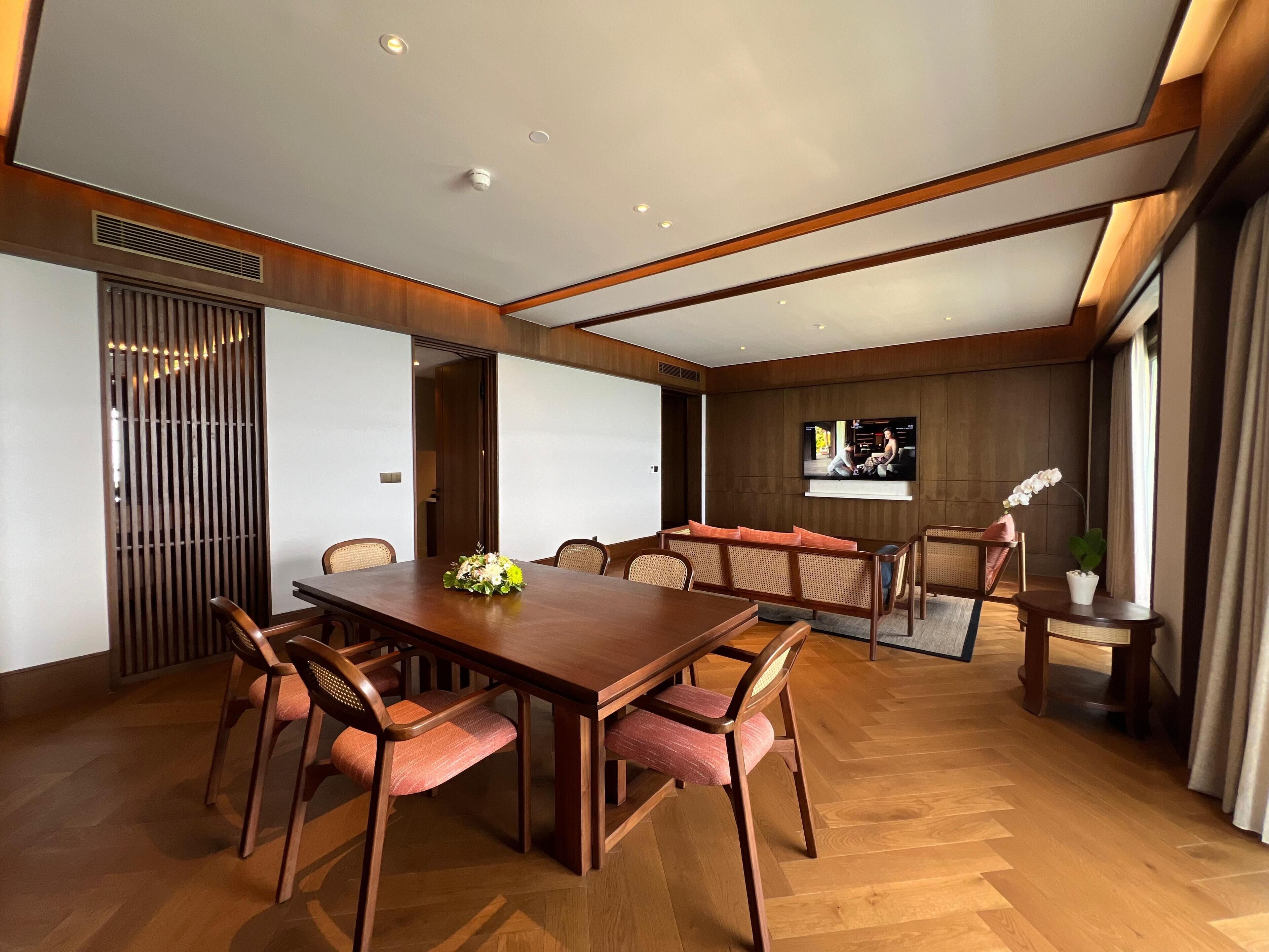 Amplia habitación con una mesa de comedor de madera, sillas acolchadas, un televisor grande en la pared y una orquídea en maceta sobre una mesita.