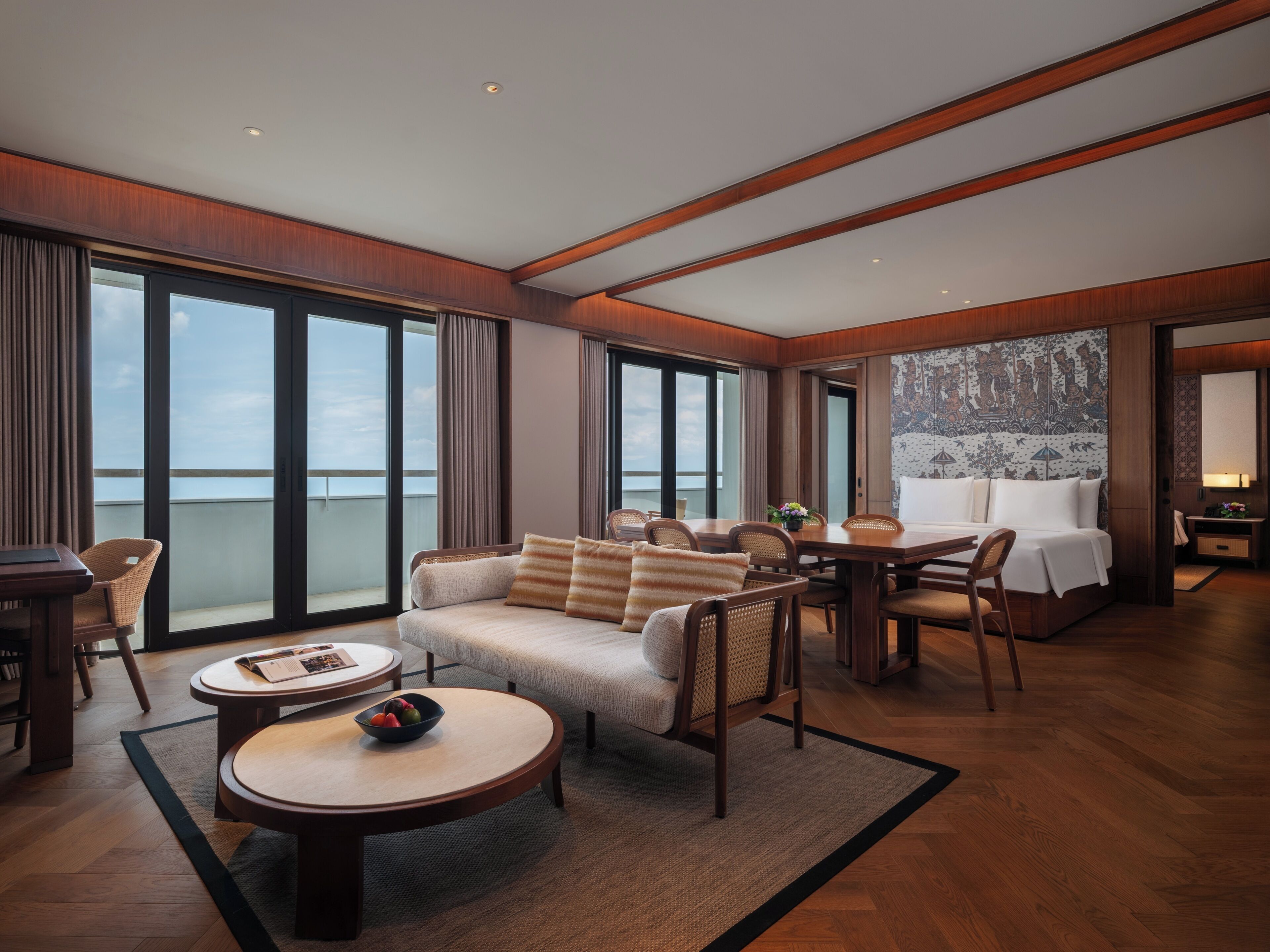 A spacious hotel room with a large bed, a sofa, a dining table, and a view of the sea.