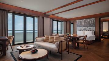 A spacious hotel room with a large bed, a sofa, a dining table, and a view of the sea.