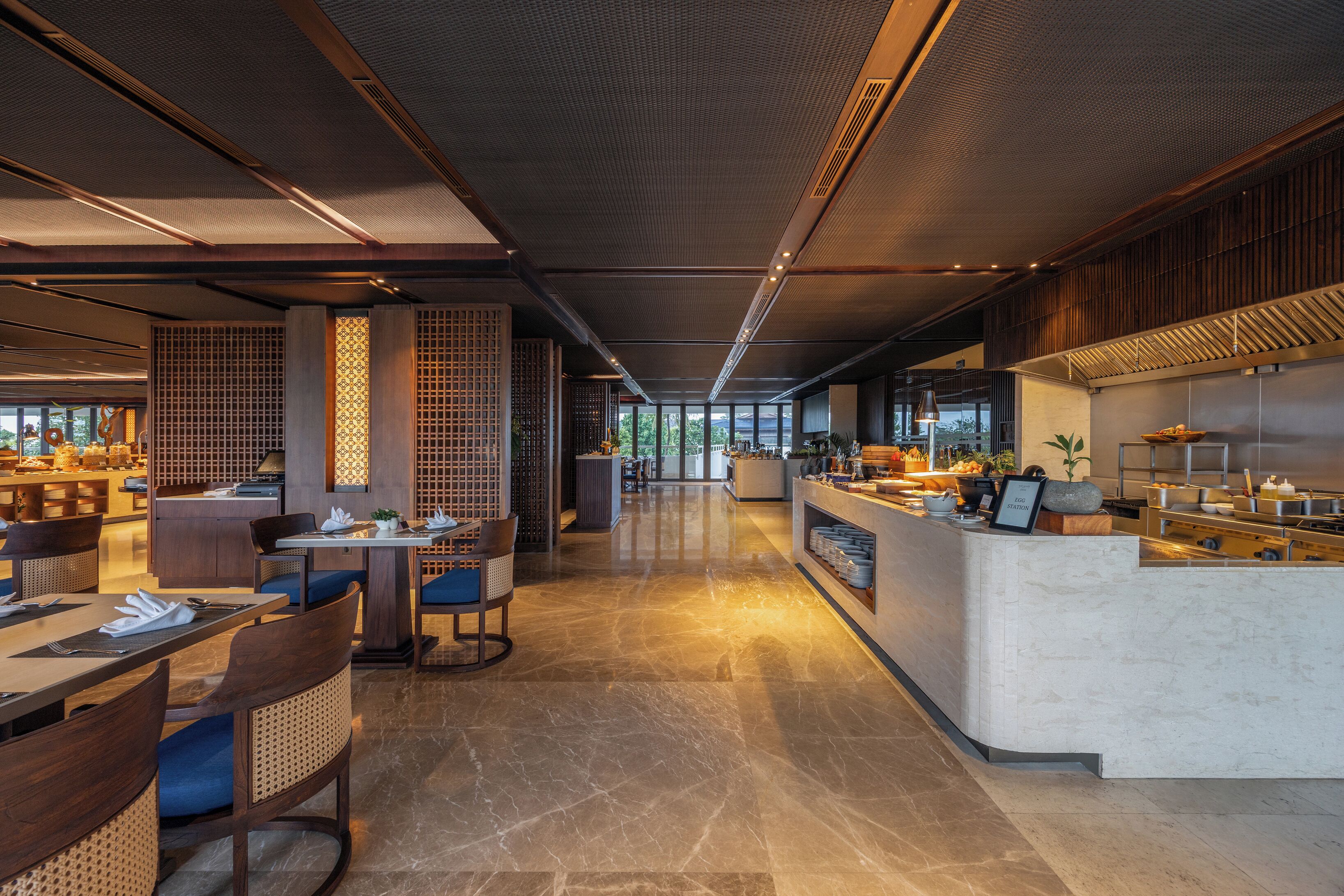 A modern restaurant with a long counter, seating area, and a kitchen visible in the background.