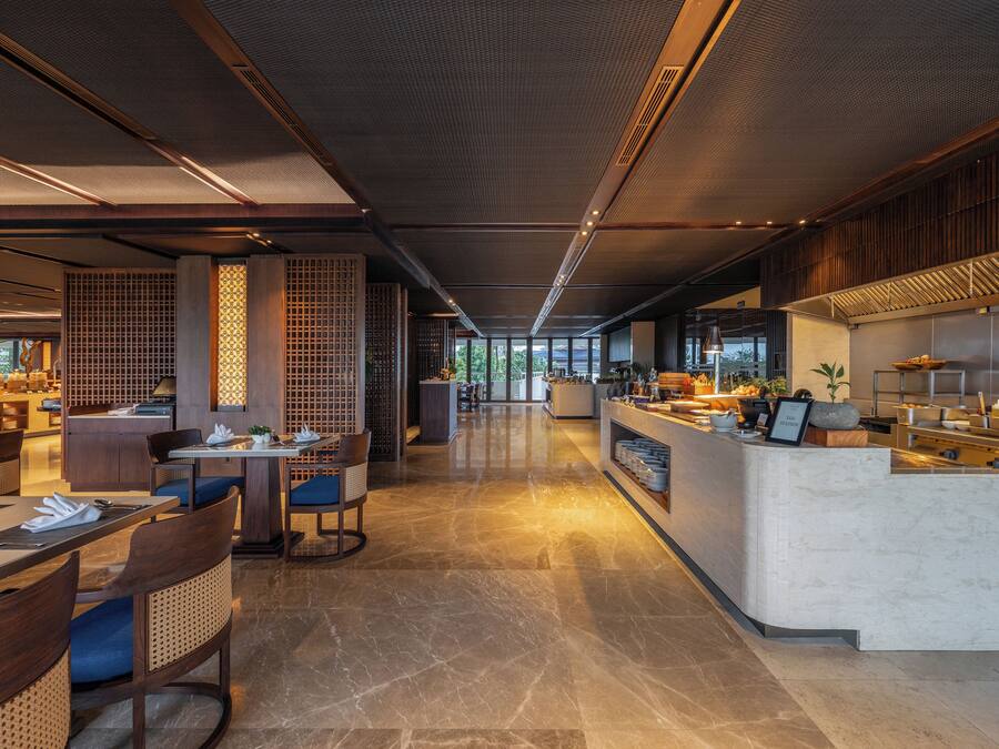 A modern restaurant with a long counter, seating area, and a kitchen visible in the background.