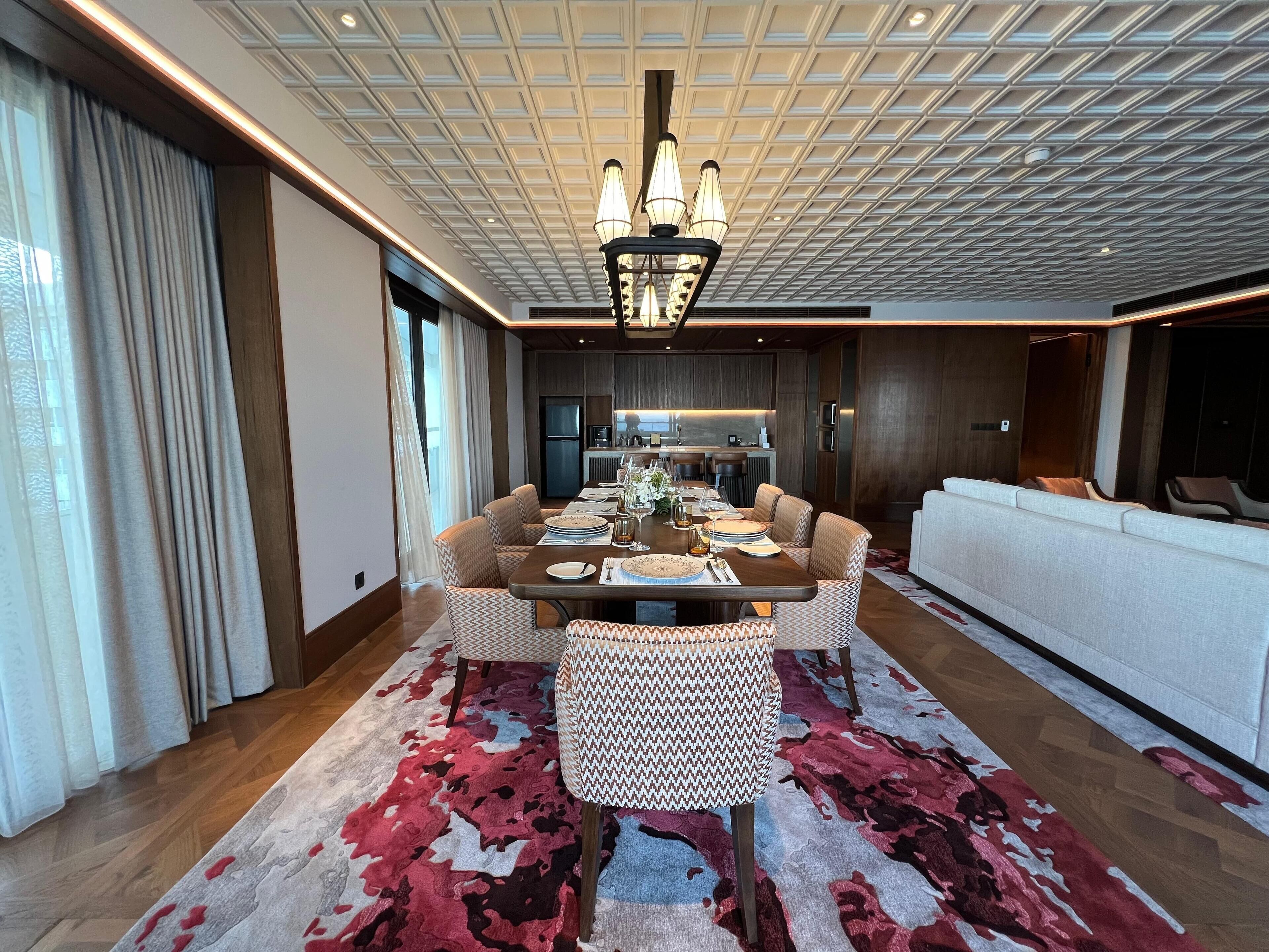 A modern dining area with a central table, patterned chairs, and a chandelier.