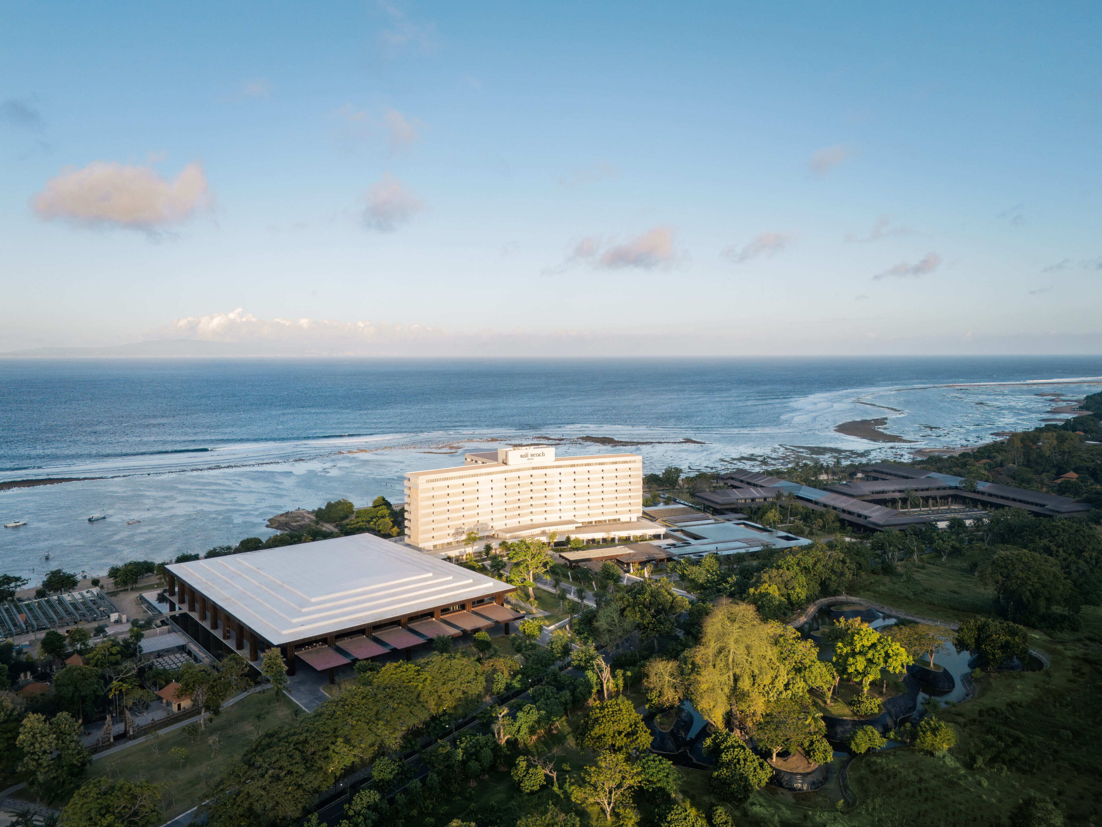 Un hôtel situé sur la côte, composé d’un grand bâtiment et d’une construction plus petite, entouré de verdure et offrant une vue sur la mer.