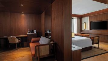 Habitación de hotel con interior de madera, una cama, un escritorio con silla, un sofá y un televisor montado en la pared.