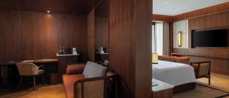 A hotel room with a wooden interior, a bed, a desk with a chair, a sofa, and a TV mounted on the wall.