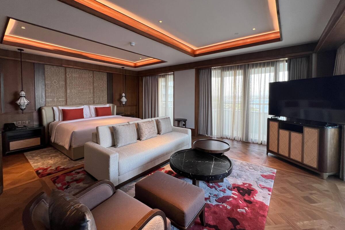 A modern hotel room with a large bed, a sofa, a TV, and a dining area.