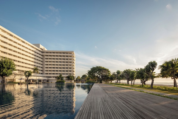 Un hotel con una piscina grande, una terraza de madera y vista al mar.