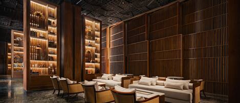 A modern lobby with a central seating area, wooden paneling, and illuminated shelves.