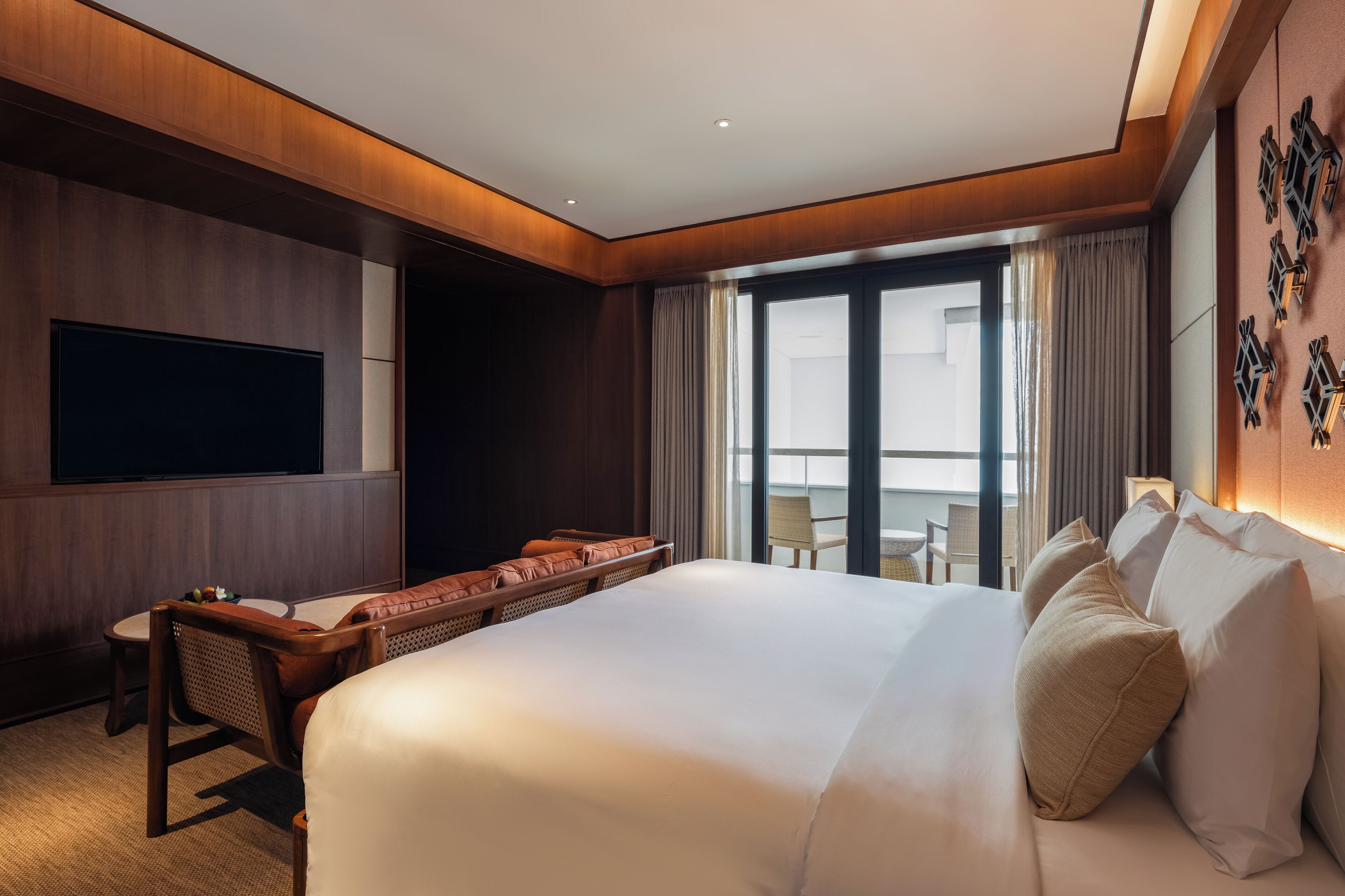 A hotel room with a large bed, a flat-screen TV, a desk with a chair, and a balcony with a table and chairs.