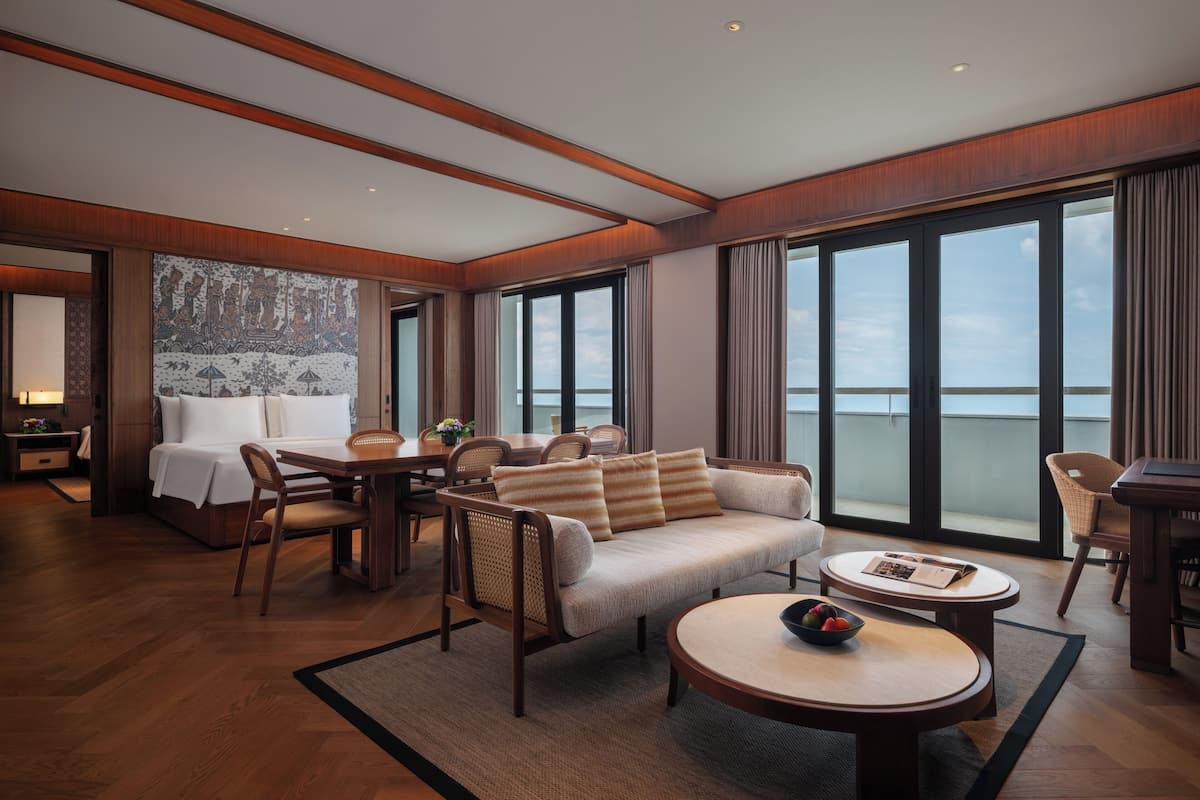 A modern hotel room with a large bed, a sofa, a dining table, and a balcony with a view.