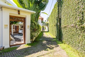 A cobblestone pathway leading to a building with a white facade and a wooden entrance. - Villa Ku Tama by Villa Finder (Seminyak)