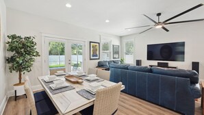 A modern living room with a sofa, dining table, and a ceiling fan. - Luxury Retreat • Hot Tub • Private Fenced Yard (Tampa)