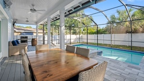 A covered outdoor area with a pool, wicker furniture, and a wooden table. - Luxury Retreat • Hot Tub • Private Fenced Yard (Tampa)