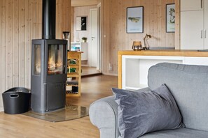 A living room with a wood-burning stove, a grey sofa, and a wooden floor.