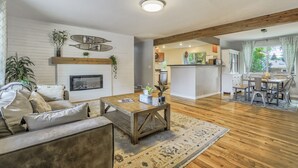 A spacious living room with a fireplace, wooden beams, a dining area, and a kitchen in the background.