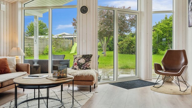Un salon spacieux doté d’une grande porte-fenêtre coulissante donnant sur un jardin, d’un canapé confortable, d’une table basse et d’un fauteuil en cuir.