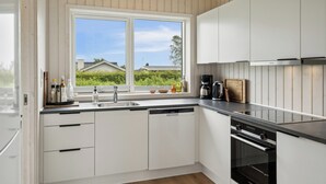 Une cuisine moderne avec des meubles blancs, un lave-vaisselle, un four et une fenêtre donnant sur un espace verdoyant.