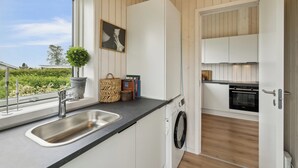 Une cuisine de taille réduite, équipée d’un évier, d’un lave-linge et d’une fenêtre donnant sur un espace verdoyant.