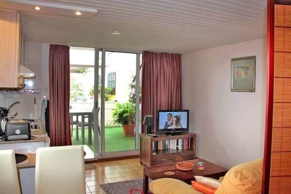 A living room with a television, a sofa, a coffee table, and a kitchen area with a stove and cabinets.