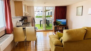 A living room with a sofa, a dining area with chairs, a kitchen with a stove, and a sliding glass door leading to an outdoor area. - Ferienapartment im Sonnigen Westen von La Palma (El Paso)