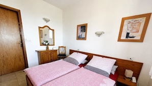 A double bed with patterned bedding, a wooden headboard, a nightstand with a lamp, a mirror, and a framed picture on the wall.