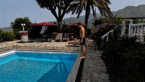 A swimming pool with a tiled edge, surrounded by lounge chairs and umbrellas, with a mountainous backdrop. - Ferienhaus im Sonnigen Westen von La Palma (El Paso)