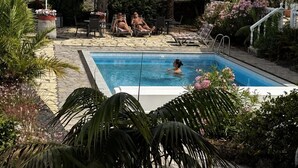 A pool area with lounge chairs and umbrellas, surrounded by palm trees and plants.