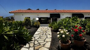 A building with a tiled roof, a stone pathway, and potted plants with flowers.