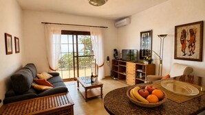 A living room with a sofa, coffee table, and a dining area with a table set for two. There is a TV, a bookshelf, and a painting on the wall. - Ferienhaus im Sonnigen Westen von La Palma (El Paso)