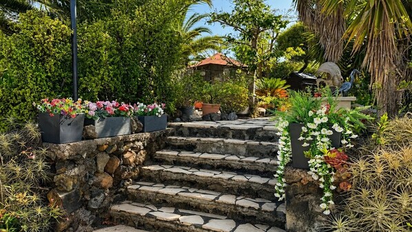 A stone staircase leading up to a building with a red roof, surrounded by lush greenery and potted plants.