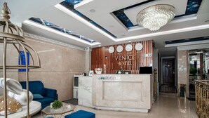 Uma área de recepção de hotel com um balcão de mármore, sofás azuis e um candelabro.